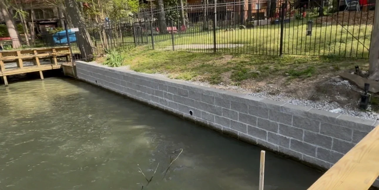 Gray concrete block retaining wall installed along waterfront with drainage provisions